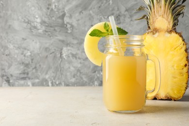 Photo of Tasty pineapple juice in mason jar, mint and slice of fresh fruit on grey textured table, closeup. Space for text