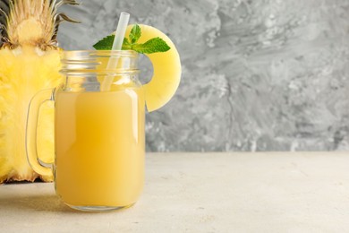 Photo of Tasty pineapple juice in mason jar, mint and slice of fresh fruit on grey textured table, closeup. Space for text