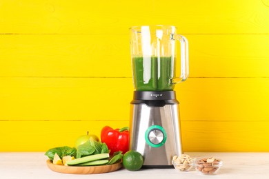 Modern blender with smoothie and ingredients on light wooden table