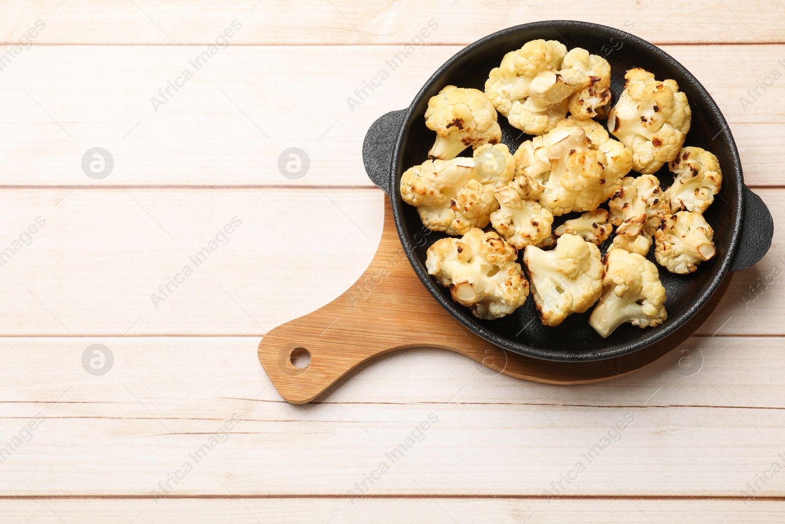 Photo of Tasty baked cauliflower in baking pan on light wooden table, top view. Space for text