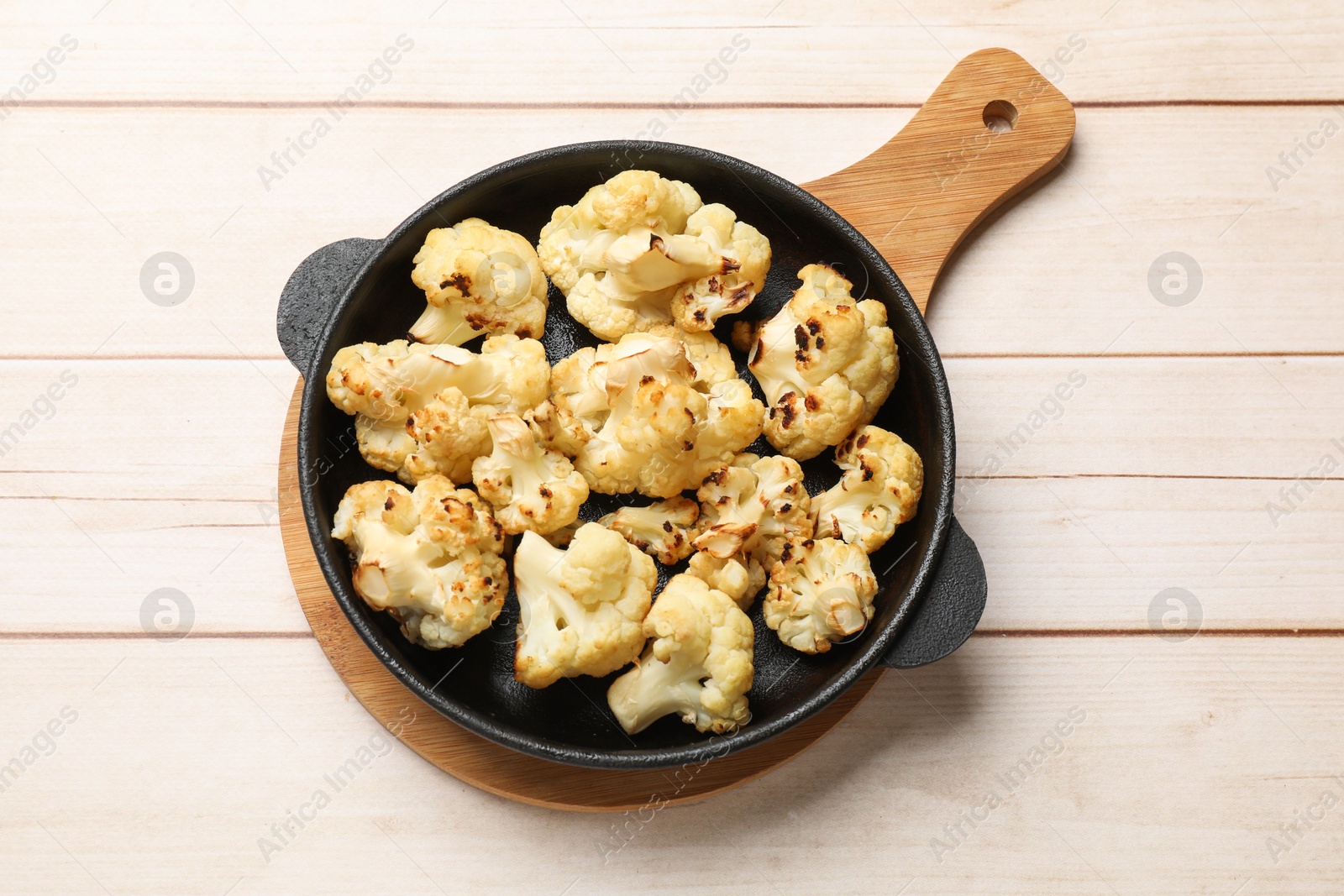 Photo of Tasty baked cauliflower in baking pan on light wooden table, top view