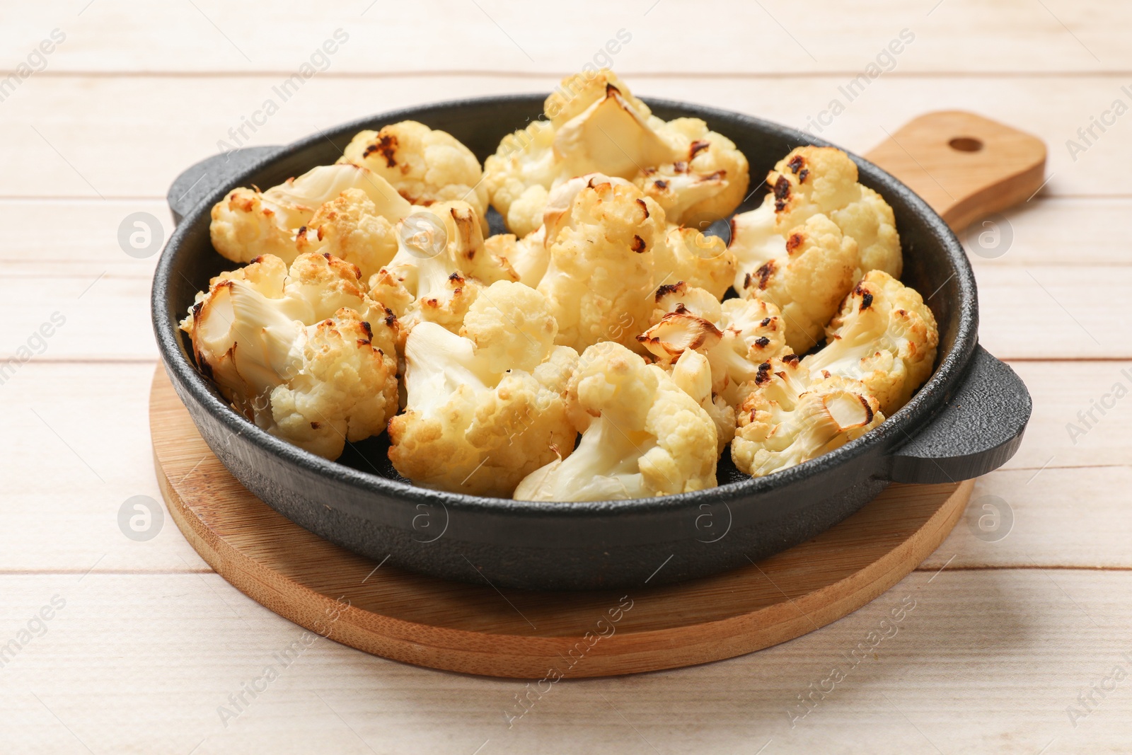 Photo of Tasty baked cauliflower in baking pan on light wooden table, closeup