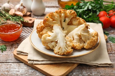 Photo of Plate with tasty baked cauliflower, sauce and products on wooden table, closeup