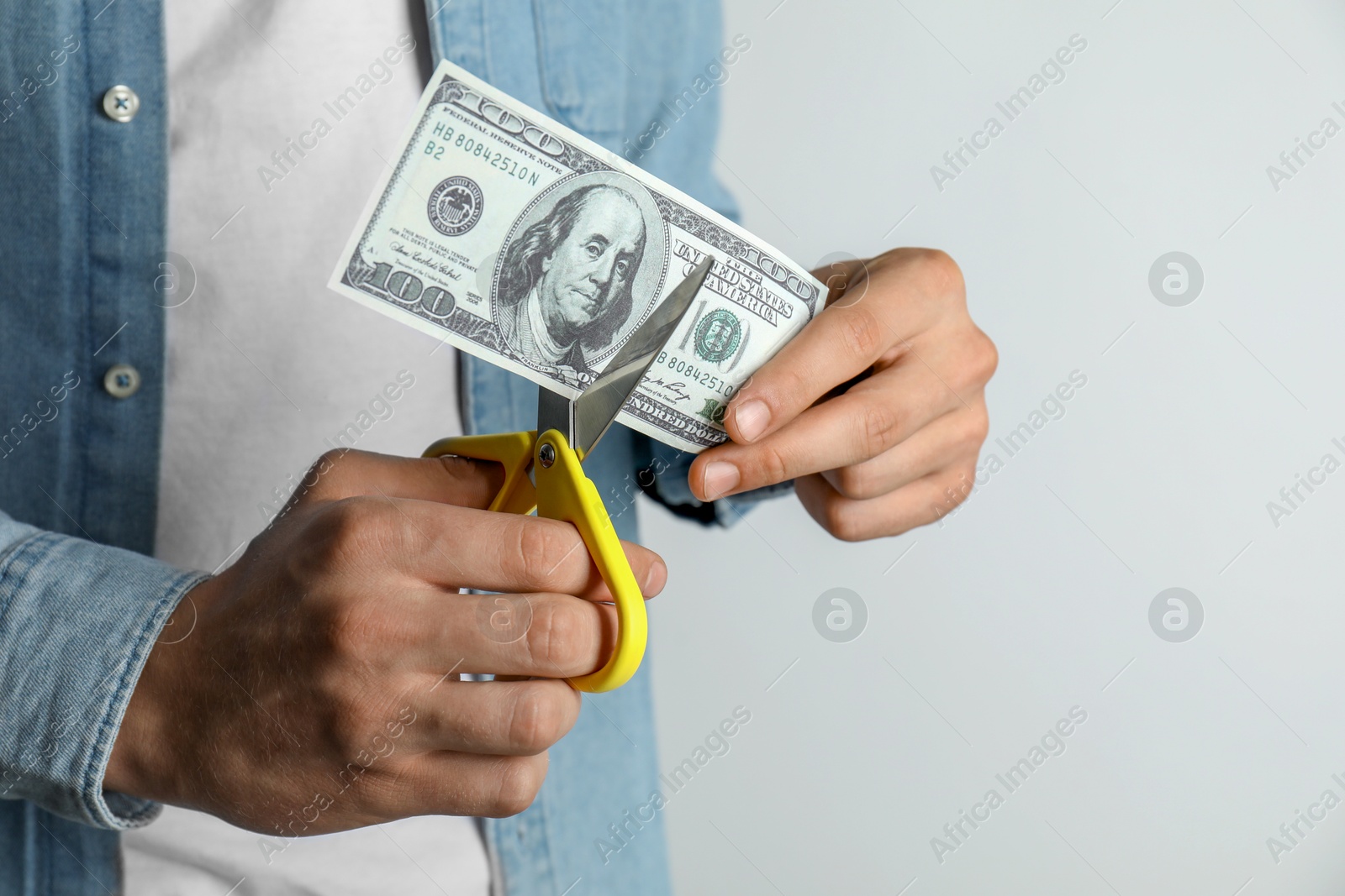 Photo of Budgeting. Man cutting dollar banknote with scissors on light grey background, closeup. Space for text