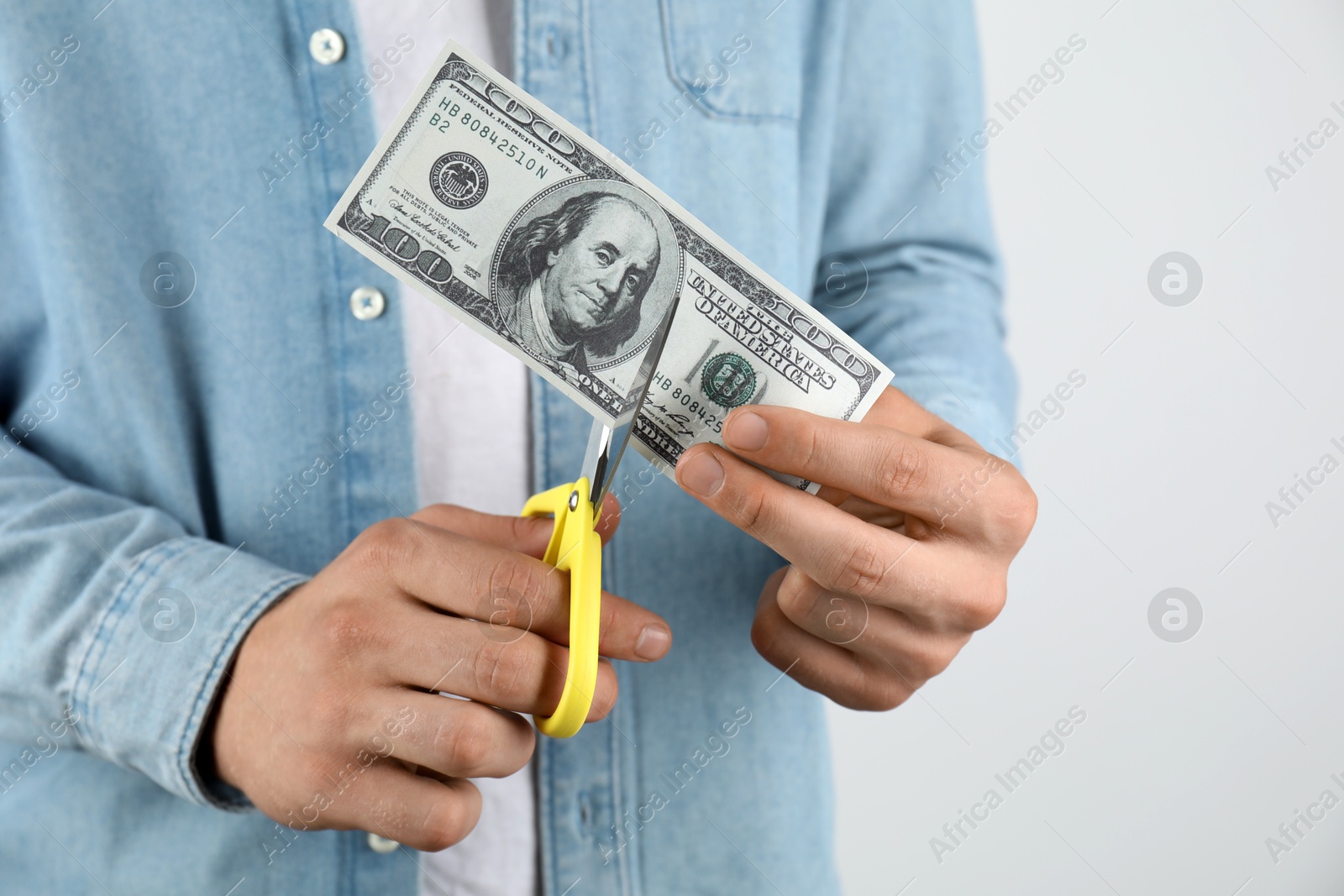 Photo of Budgeting. Man cutting dollar banknote with scissors on light grey background, closeup