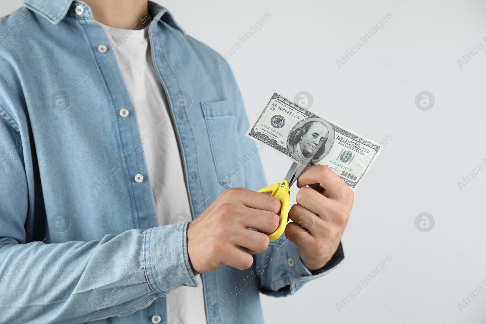 Photo of Budgeting. Man cutting dollar banknote with scissors on light grey background, closeup