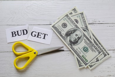 Cut paper with word Budget, dollar banknotes and scissors on white wooden table, top view