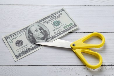 Photo of Budgeting. Dollar banknote with scissors on white wooden table, top view