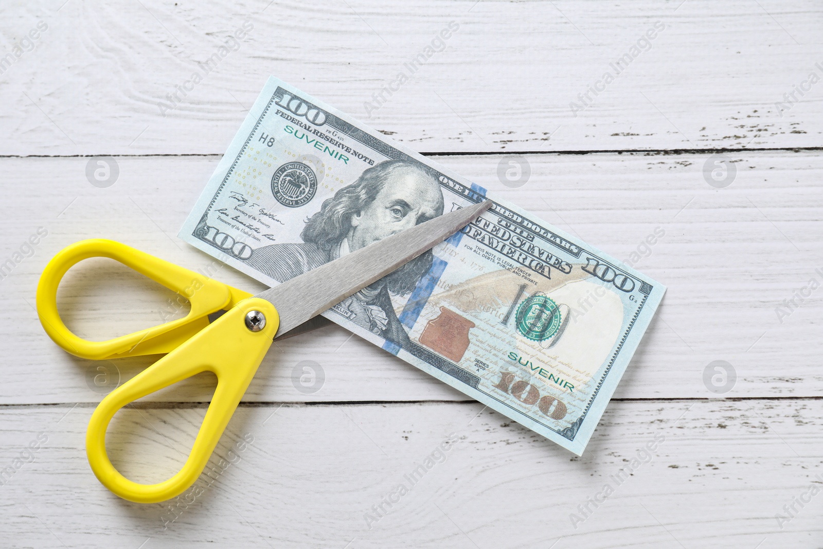 Photo of Budgeting. Dollar banknote with scissors on white wooden table, top view