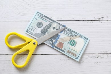 Photo of Budgeting. Dollar banknote with scissors on white wooden table, top view