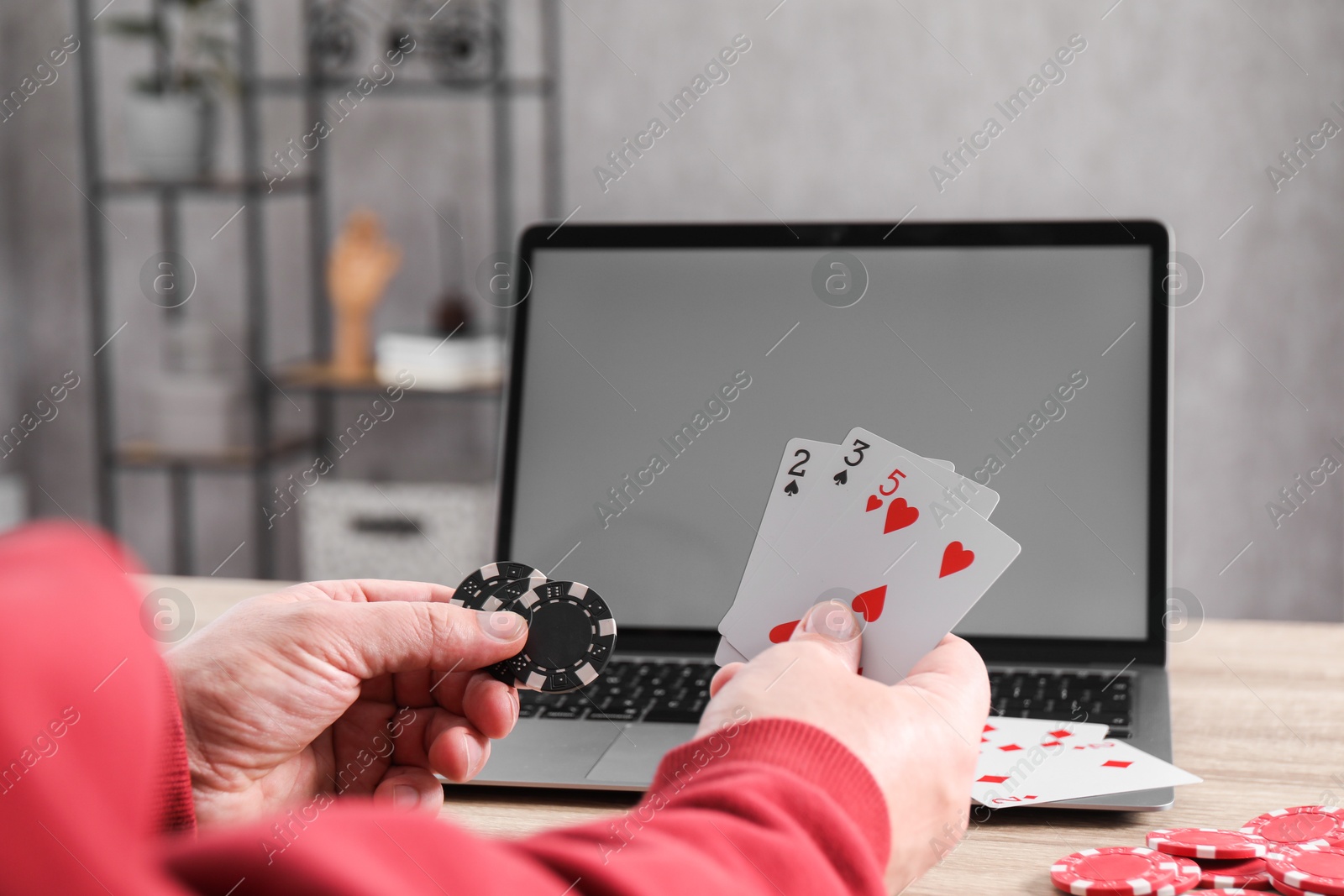 Photo of Online poker. Man with playing cards, chips and laptop at wooden table indoors, closeup