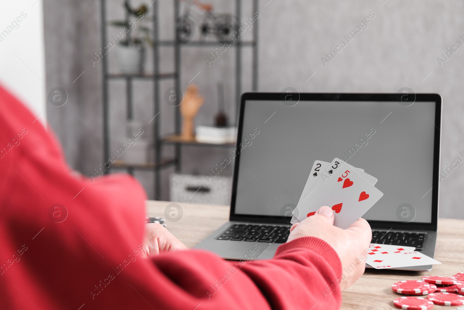 Photo of Online poker. Man with playing cards, chips and laptop at wooden table indoors, closeup