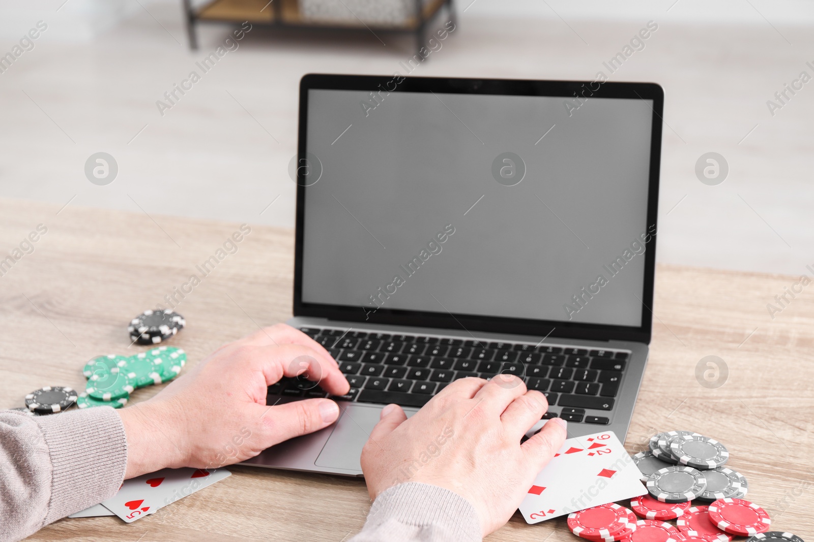 Photo of Online poker. Man with playing cards and chips using laptop at wooden table indoors, closeup