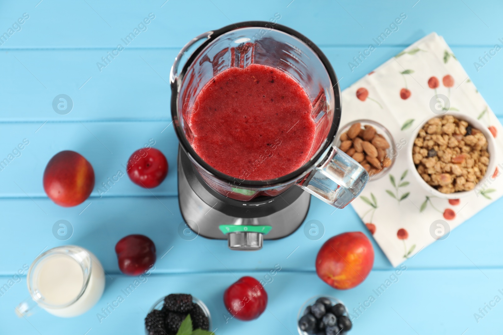 Photo of Blender with mixture of ingredients and other fresh products on light blue wooden table, top view