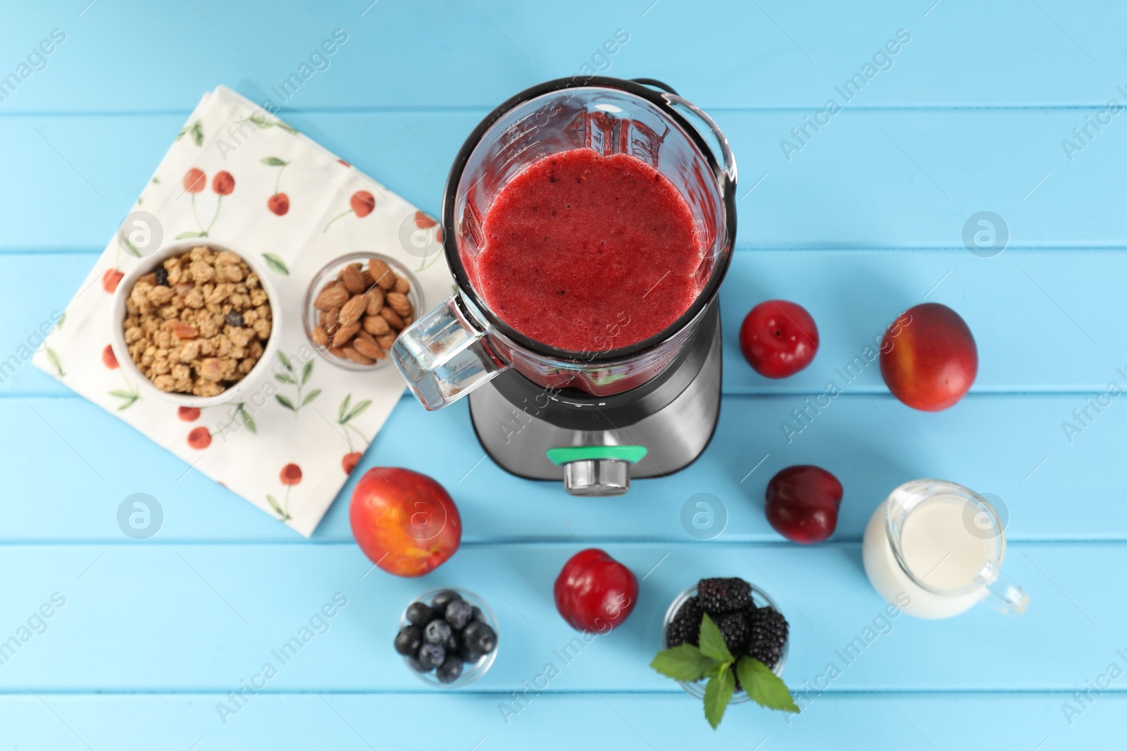 Photo of Blender with mixture of ingredients and other fresh products on light blue wooden table, above view