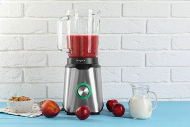 Photo of Blender with mixture of ingredients and other fresh products on light blue wooden table