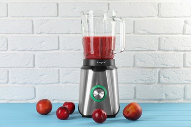 Photo of Blender with mixture of ingredients and fresh fruits on light blue wooden table