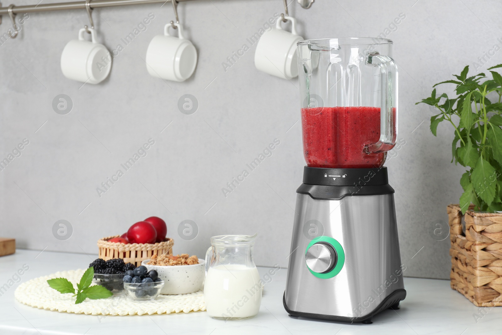 Photo of Blender with mixture of ingredients and other fresh products on white countertop in kitchen