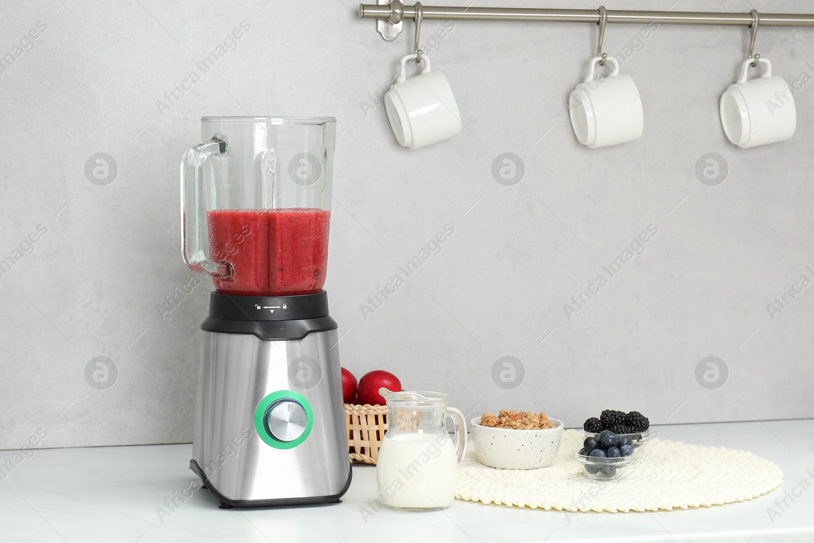 Photo of Blender with mixture of ingredients and other fresh products on white countertop in kitchen