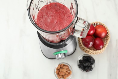 Photo of Blender with mixture of ingredients and other fresh products on white marble table, above view