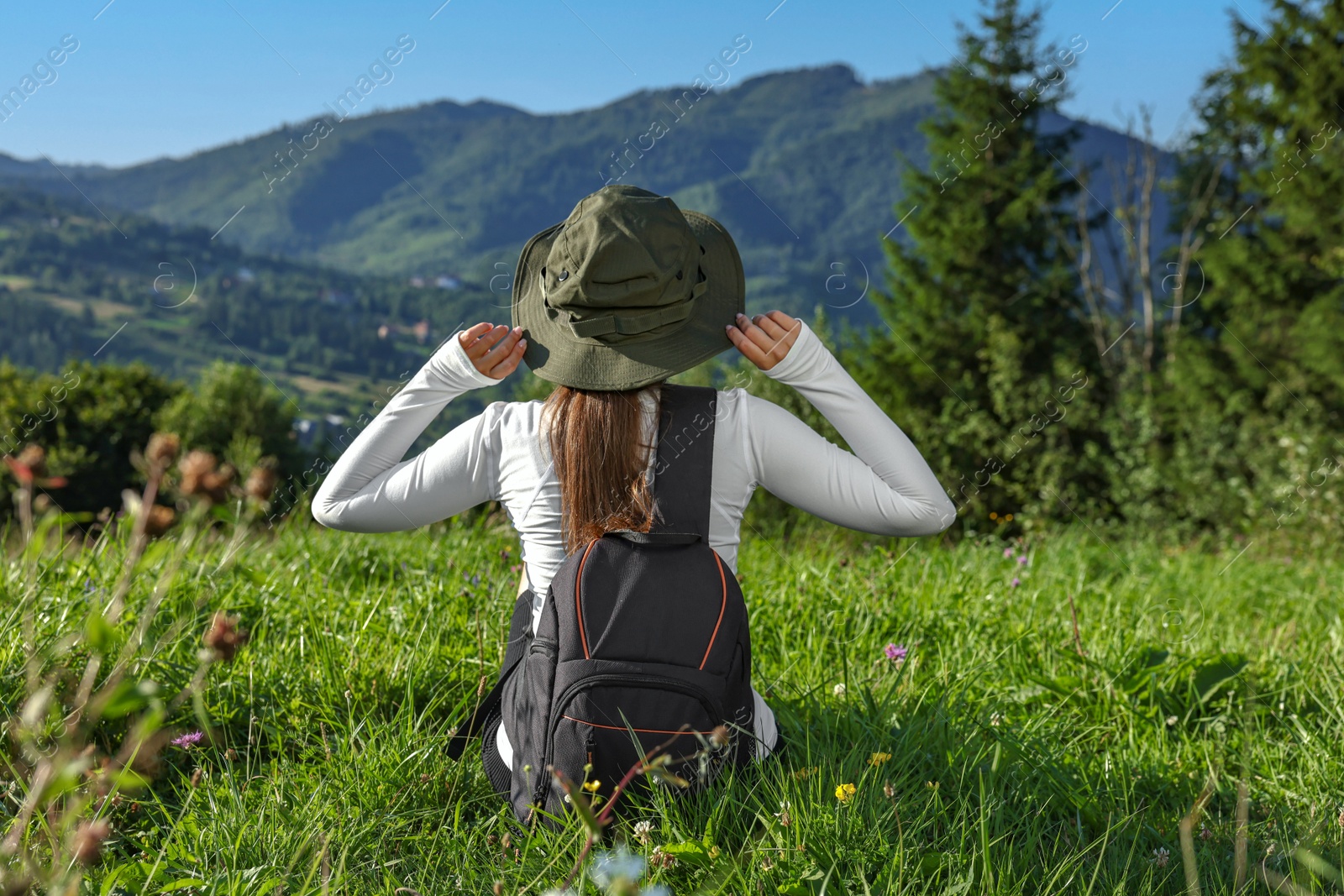 Photo of Woman with backpack on green grass in beautiful mountains, back view