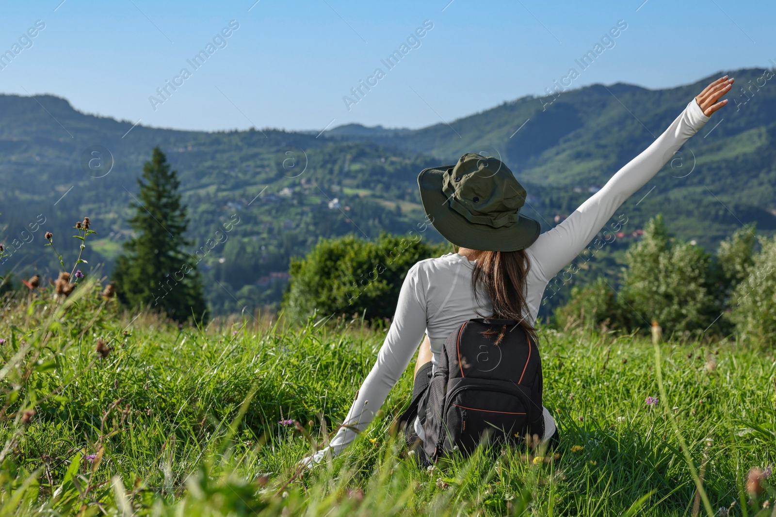 Photo of Woman with backpack on green grass in beautiful mountains, back view