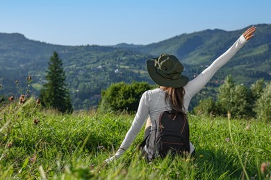 Woman with backpack on green grass in beautiful mountains, back view