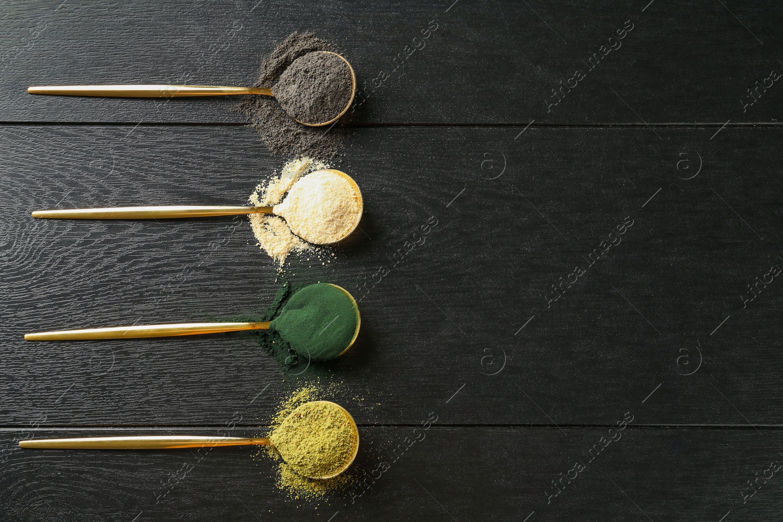 Photo of Different superfood powders in spoons on black wooden table, flat lay. Space for text