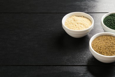 Photo of Different healthy superfoods in bowls on black wooden table, space for text