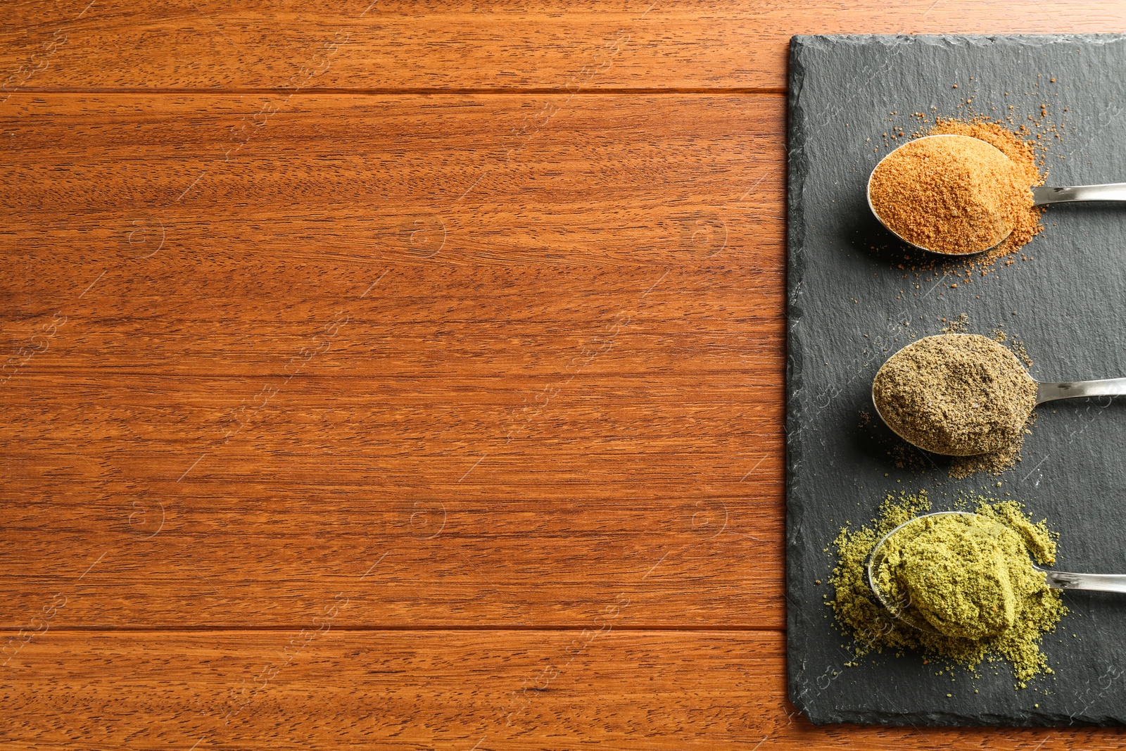 Photo of Different superfood powders in spoons on wooden table, top view. Space for text