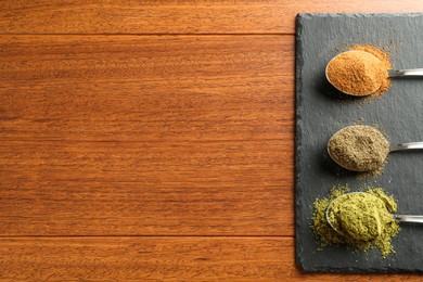 Photo of Different superfood powders in spoons on wooden table, top view. Space for text