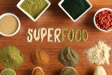 Photo of Word Superfood and different healthy powders on wooden table, flat lay