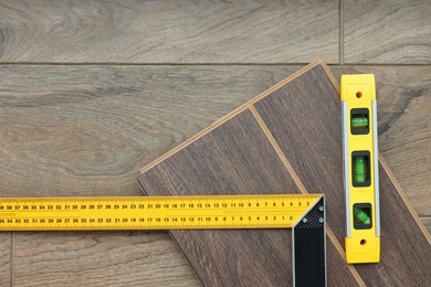 Photo of Angle ruler, level tool and laminate flooring pieces on wooden surface, top view