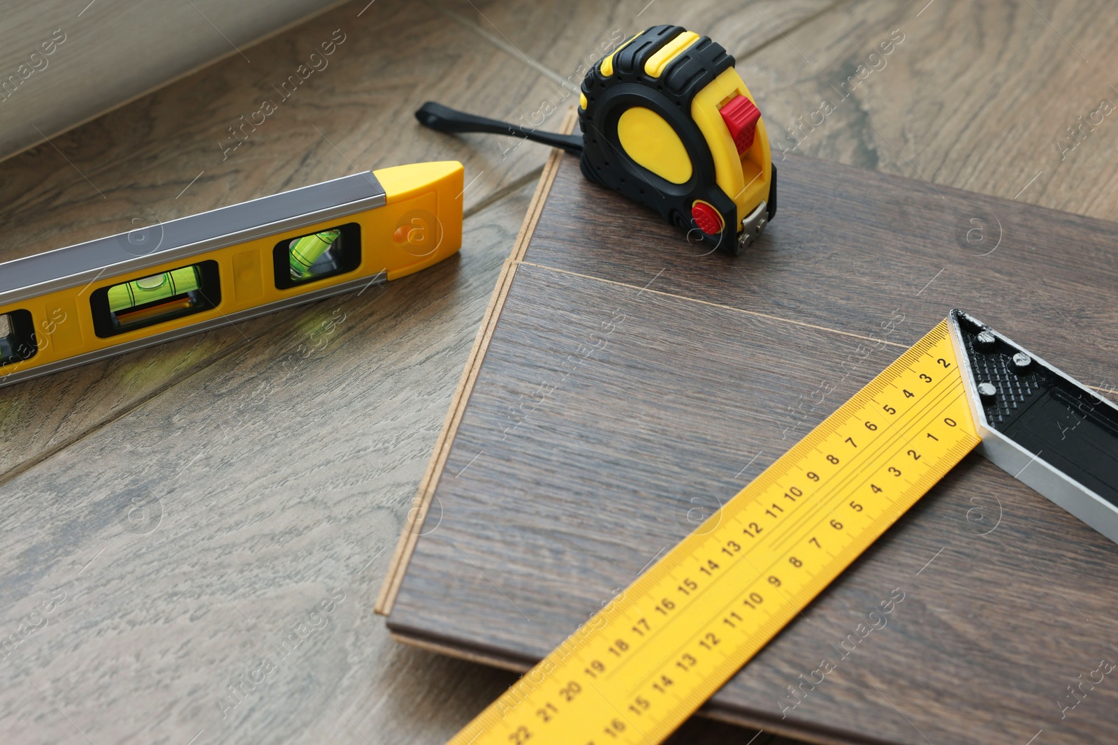 Photo of Measuring tools and laminate flooring pieces on wooden surface, closeup