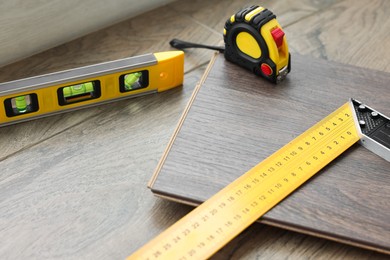 Photo of Measuring tools and laminate flooring pieces on wooden surface, closeup