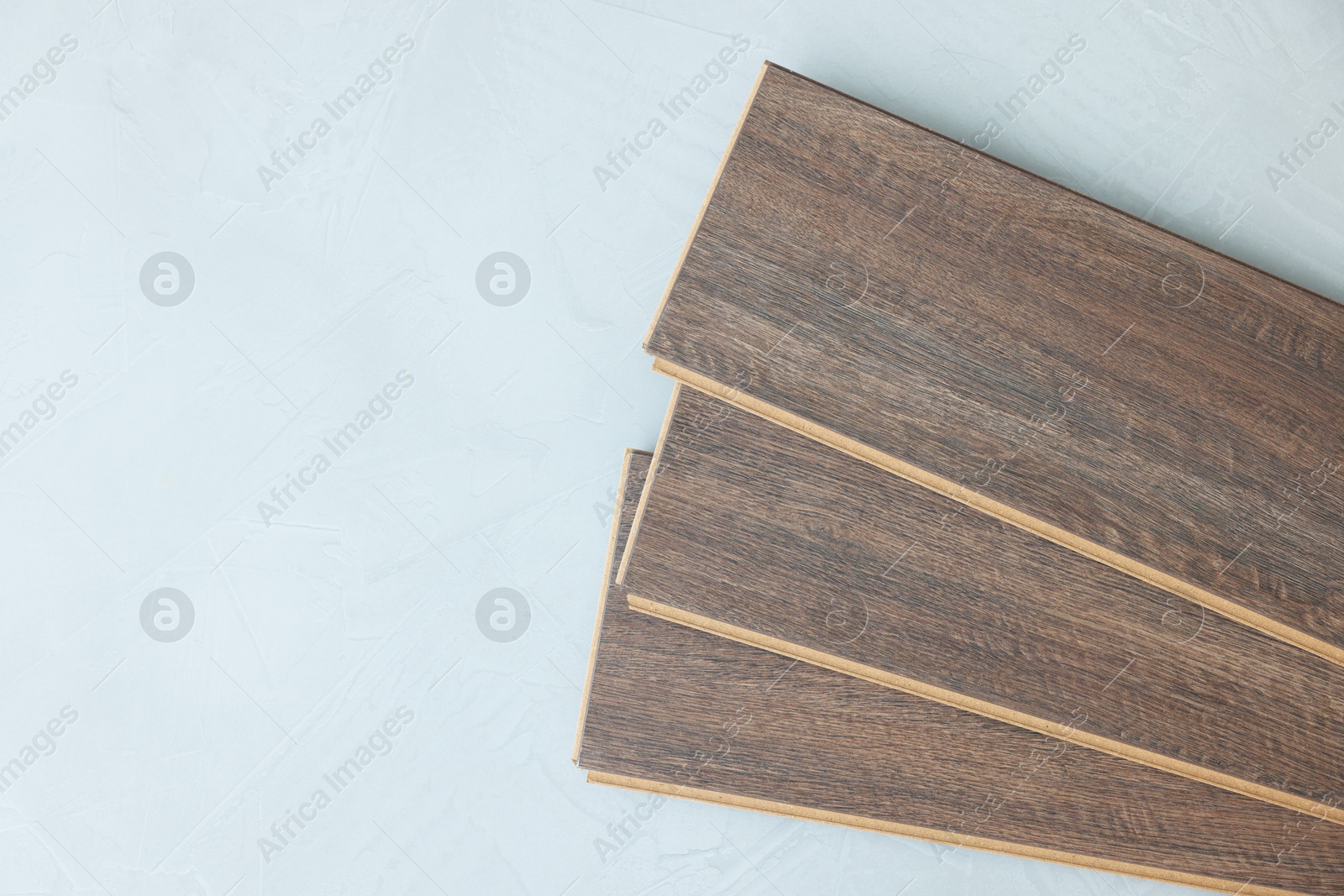 Photo of Laminate flooring pieces on grey textured surface, top view. Space for text