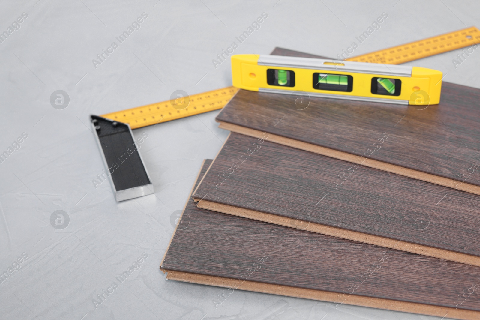 Photo of Angle ruler, level tool and laminate flooring pieces on grey textured surface, closeup