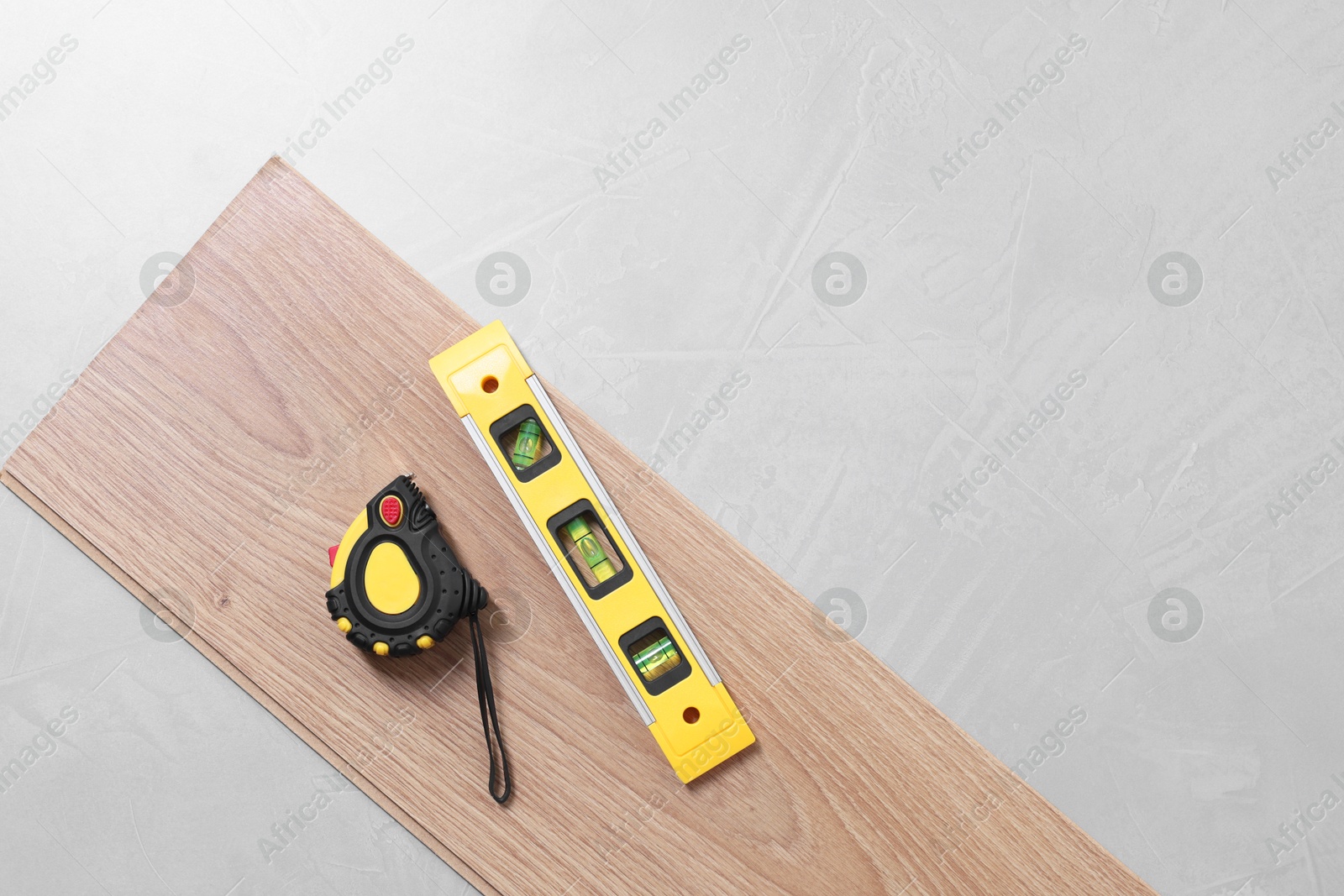 Photo of Different measuring tools and laminate flooring piece on grey textured surface, top view. Space for text