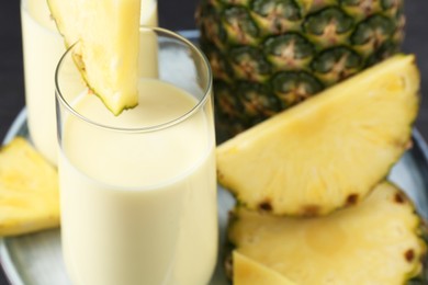 Photo of Tasty pineapple smoothie in glasses and fruit on plate, closeup