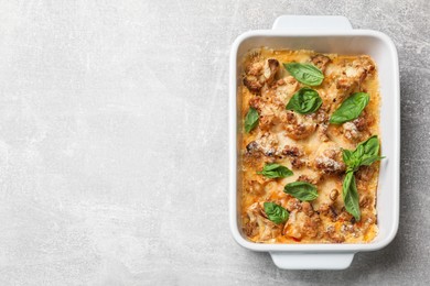 Tasty baked cauliflower and basil in baking dish on light grey table, top view. Space for text