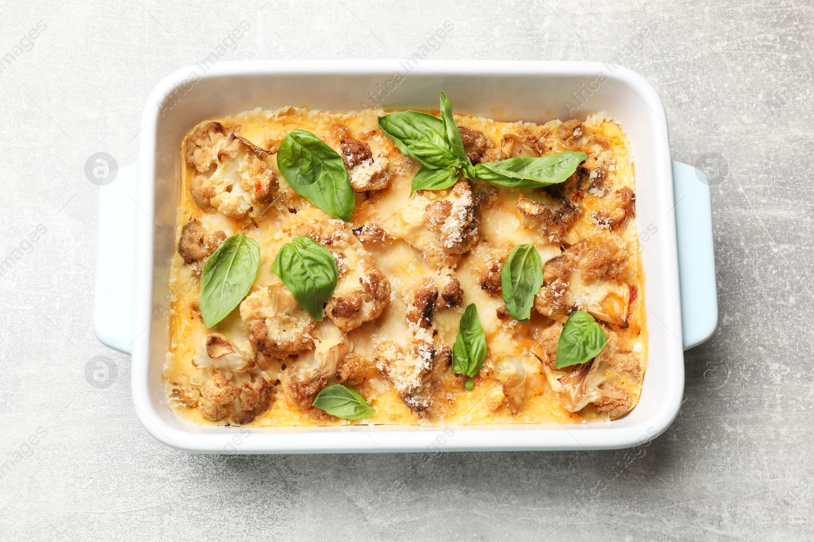 Photo of Tasty baked cauliflower and basil in baking dish on light grey table, top view