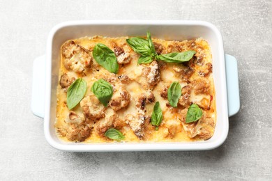 Photo of Tasty baked cauliflower and basil in baking dish on light grey table, top view