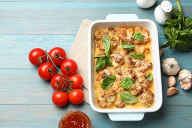 Tasty baked cauliflower in baking dish, basil, garlic, tomatoes and sauce on light blue wooden table, top view