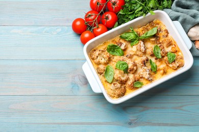 Tasty baked cauliflower in baking dish, basil, parsley, garlic and tomatoes on light blue wooden table, top view. Space for text