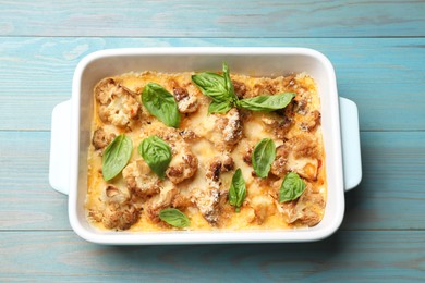 Photo of Tasty baked cauliflower and basil in baking dish on light blue wooden table, top view