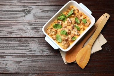 Tasty baked cauliflower and basil in baking dish on wooden table, top view. Space for text