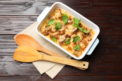 Tasty baked cauliflower and basil in baking dish on wooden table, top view