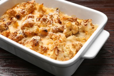 Photo of Tasty baked cauliflower in baking dish on wooden table, closeup