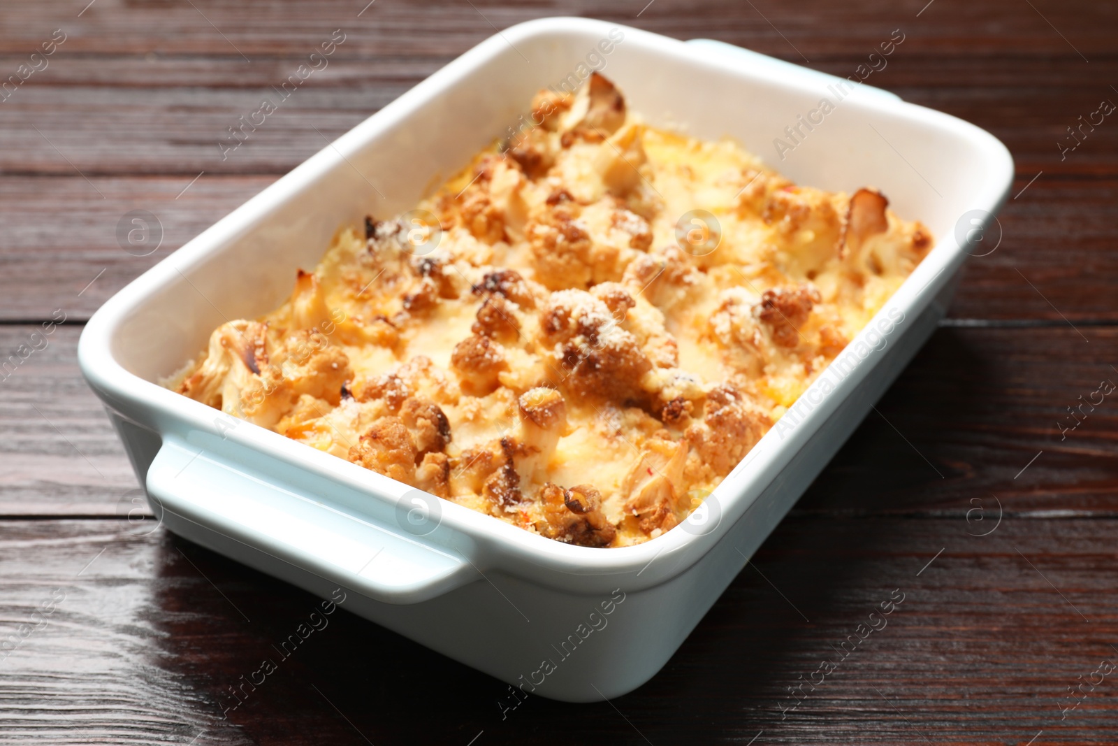 Photo of Tasty baked cauliflower in baking dish on wooden table, closeup