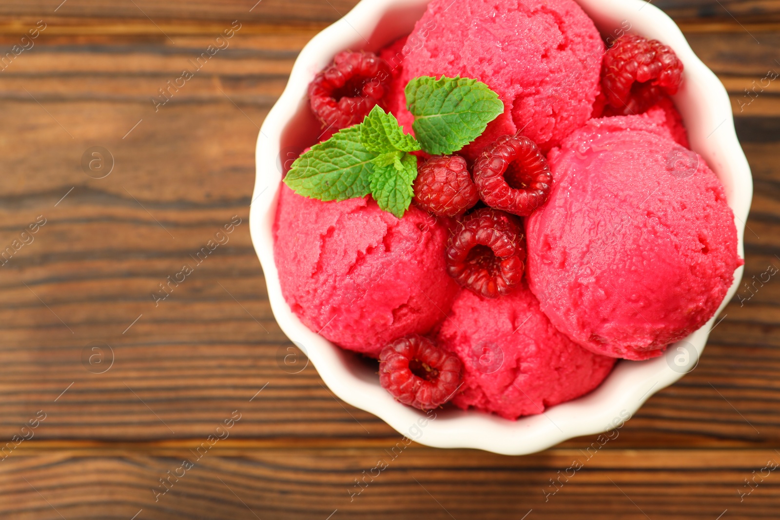 Photo of Delicious raspberry sorbet, fresh berries and mint in bowl on wooden table, top view